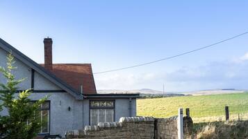 A house with a stone wall, a chimney, and a view of a green field.