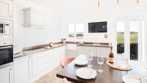 A modern kitchen with white cabinetry, a wooden countertop, and a dining area set for two with a bottle of wine and glasses. - Northern Hideaways, Sunnyside, Otterburn (Newcastle-upon-Tyne)