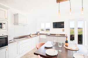 Una cocina moderna con armarios blancos, encimera de madera y una zona de comedor para dos personas, con una botella de vino y copas.