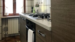 A kitchen with wooden cabinets, a stove, and a window with curtains. - Casa Olinda (Lazise)