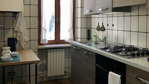 A compact kitchen with a gas stove, a sink, and wooden cabinets. - Casa Olinda (Lazise)