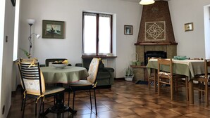 A dining area with a fireplace, a table with chairs, and a window with curtains. - Casa Olinda (Lazise)