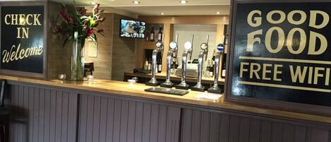 A reception area with a check-in sign, a welcome sign, a display of beer taps, and a sign advertising free WiFi.