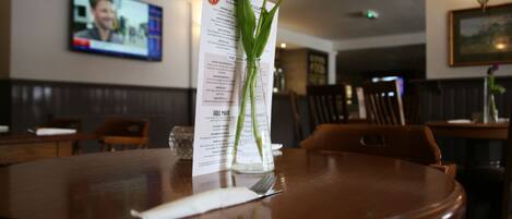 Un restaurante con una mesa de madera, un menú y un florero con una tulipa púrpura.