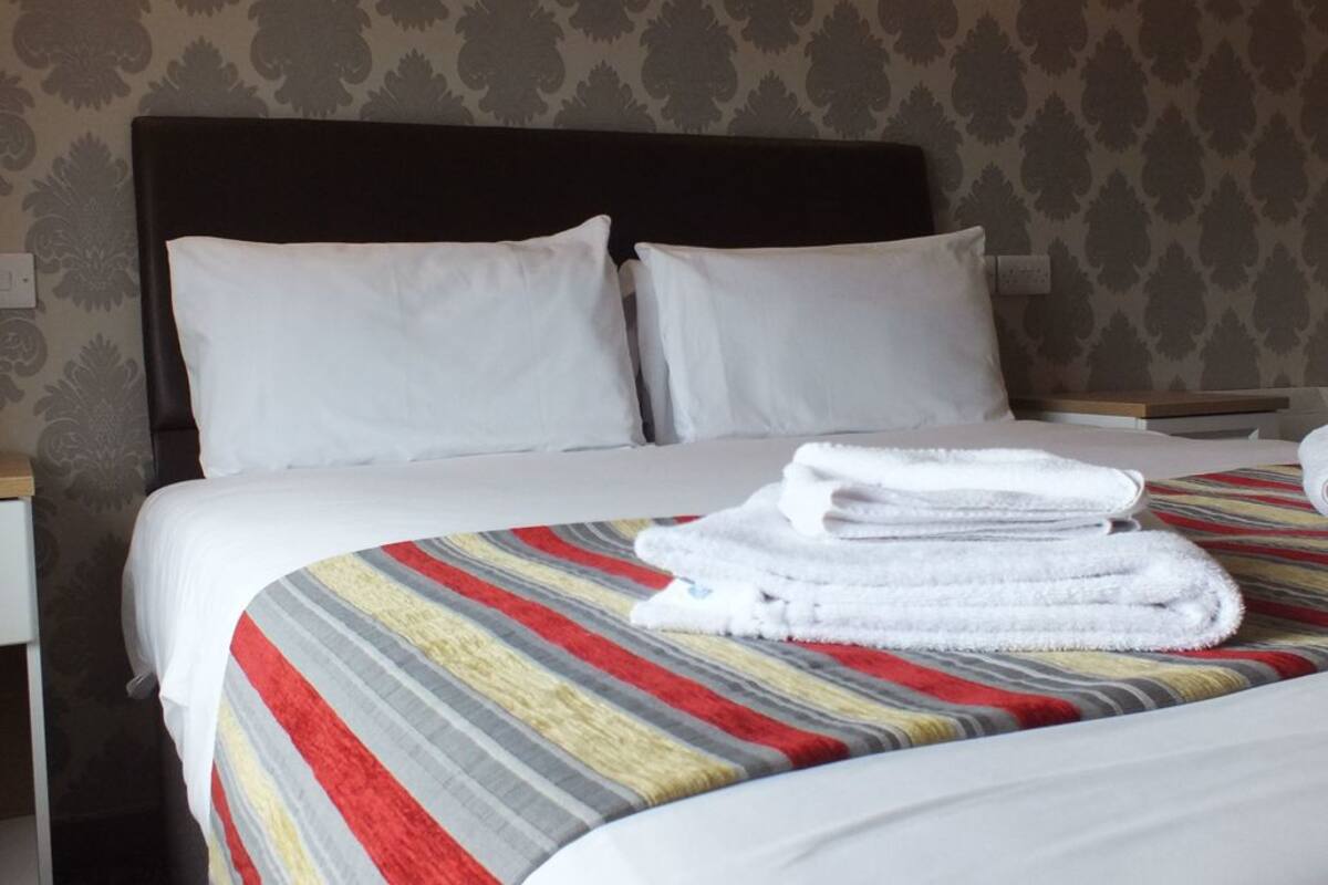 A neatly made bed with white linens and a striped blanket, a headboard, and a wall with a patterned wallpaper.