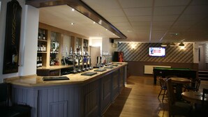 A bar area with a long counter, multiple taps, and shelves with bottles. There is a pool table and chairs in the background. - The Fazeley Inn (Tamworth)