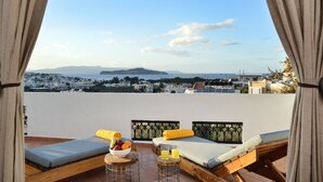 A balcony with two wooden beds, a table with fruit and drinks, and a view of a coastal town. - Villa ANVA, amazing views, walk to the beach (Daratsos)