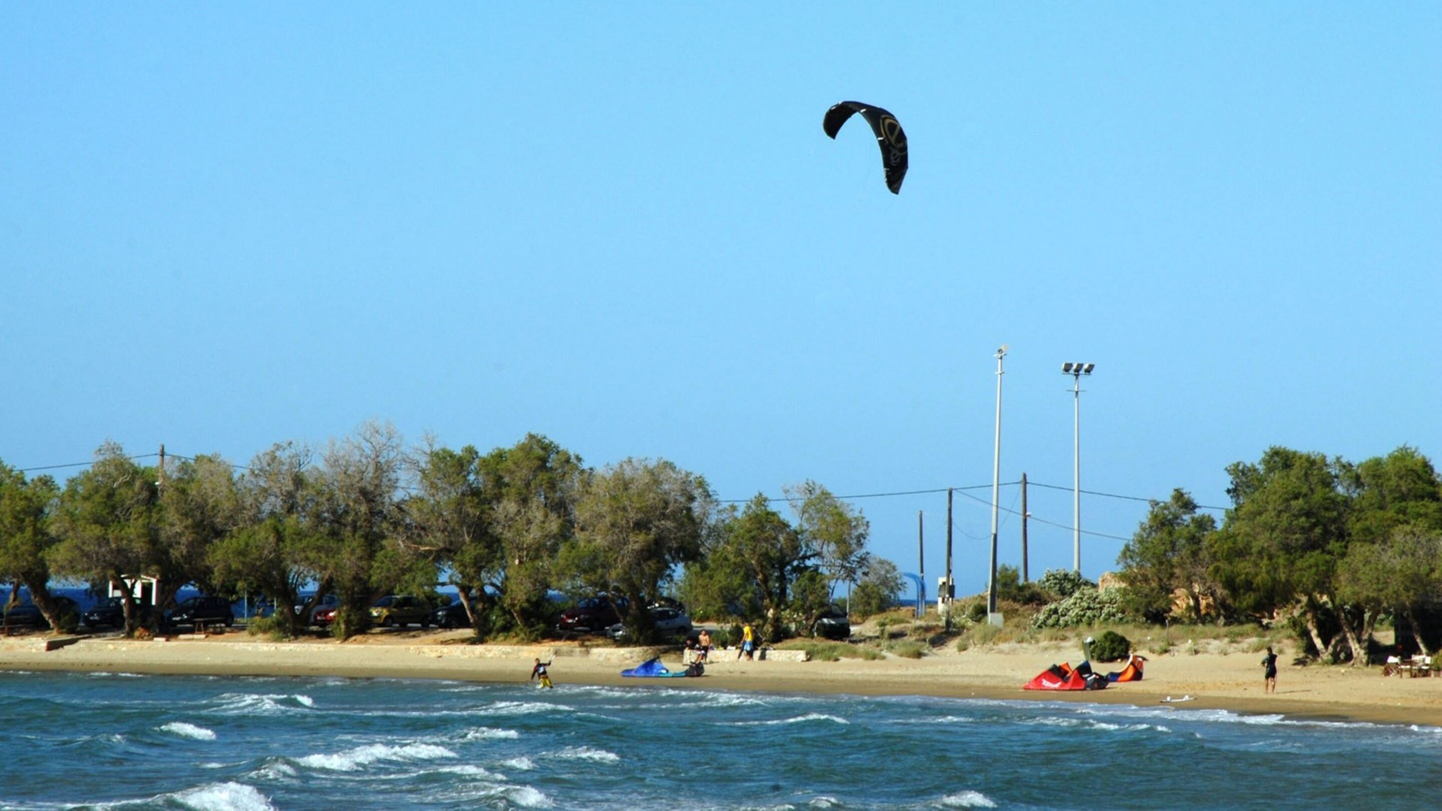 Una playa con un paracaídas en el cielo, gente en la arena y un cielo azul despejado.