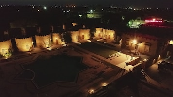 Vista nocturna de un edificio histórico con arquitectura tradicional, que incluye un amplio patio y una piscina.