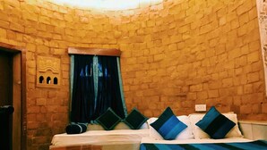 A room with a brick wall, a bed with blue and white bedding, a small table, and a window with curtains. - Himmatgarh Palace (Jaisalmer)