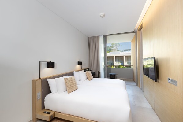 Habitación de hotel moderna con una cama grande, mesitas de noche, un televisor y un balcón con vistas.