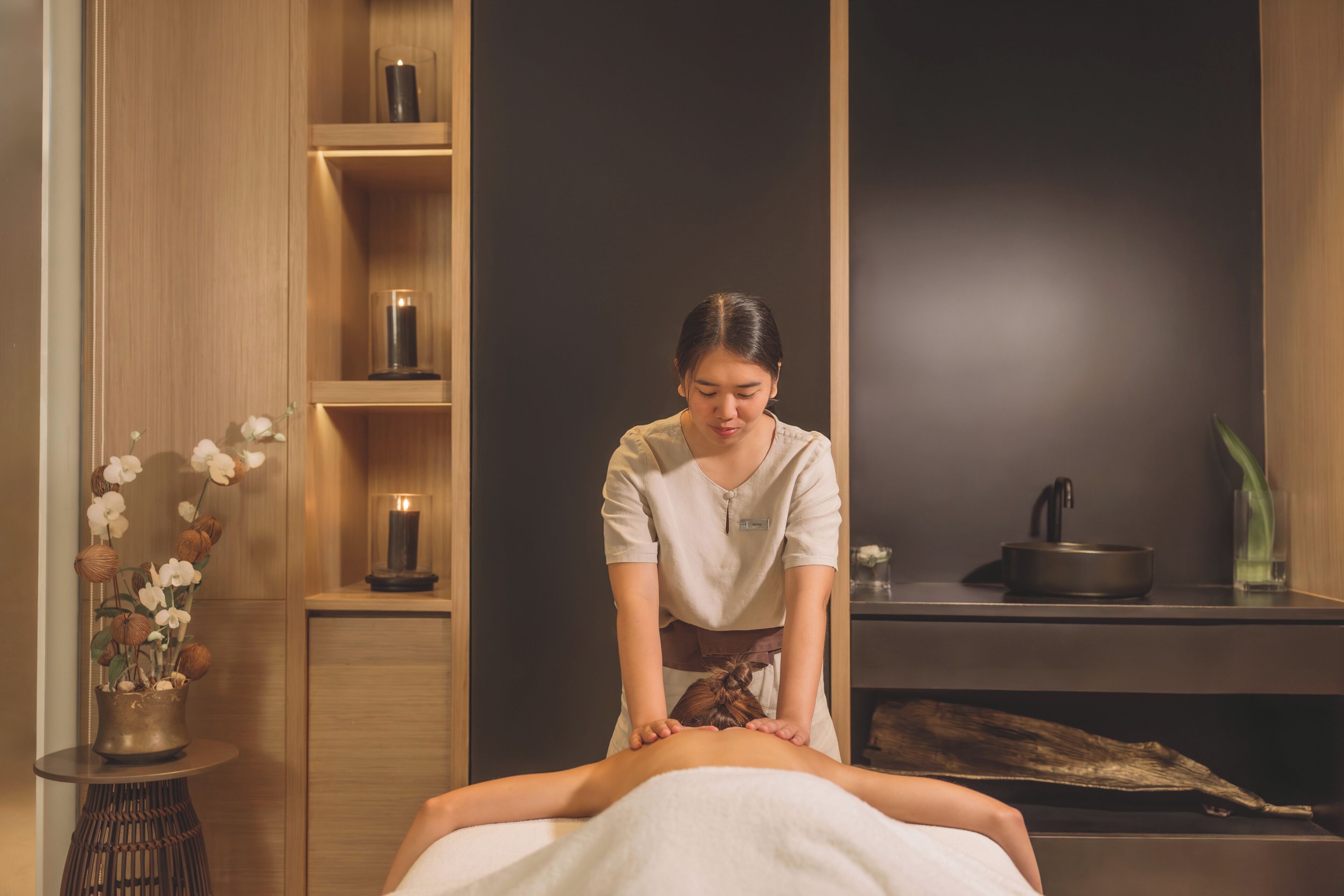A massage therapy room with a wooden cabinet, a small table with a candle, and a vase of flowers.