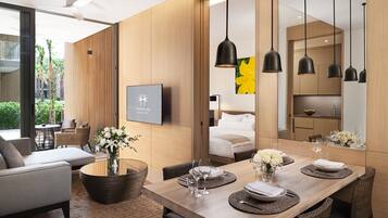 A modern dining area with a wooden table set for a meal, a sofa, and a large window overlooking greenery.