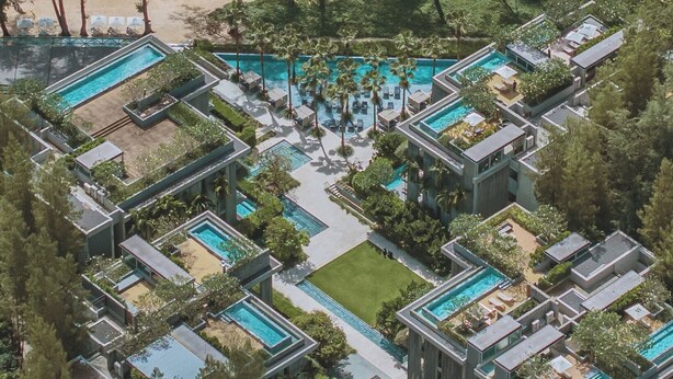 Eine Vogelperspektive zeigt ein Resort mit mehreren Schwimmbecken, Palmen und einem Strand.