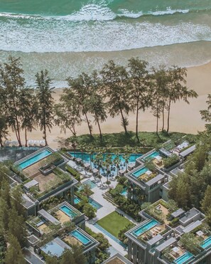 Vista aérea de un resort con múltiples piscinas, palmeras y una playa.