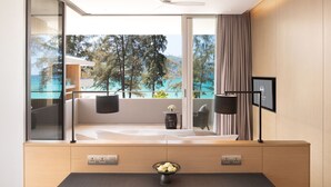 Ein modernes Hotelzimmer mit Balkon, Bett, Schreibtisch und Blick auf Meer und Bäume.