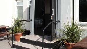 Un edificio con puerta negra, un pequeño porche con escalones y un banco de madera.