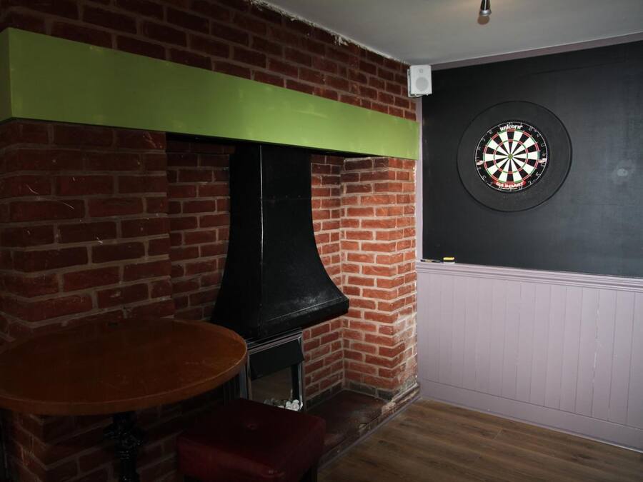 Une pièce avec une cheminée en briques, un jeu de fléchettes accroché au mur et une table ronde en bois.