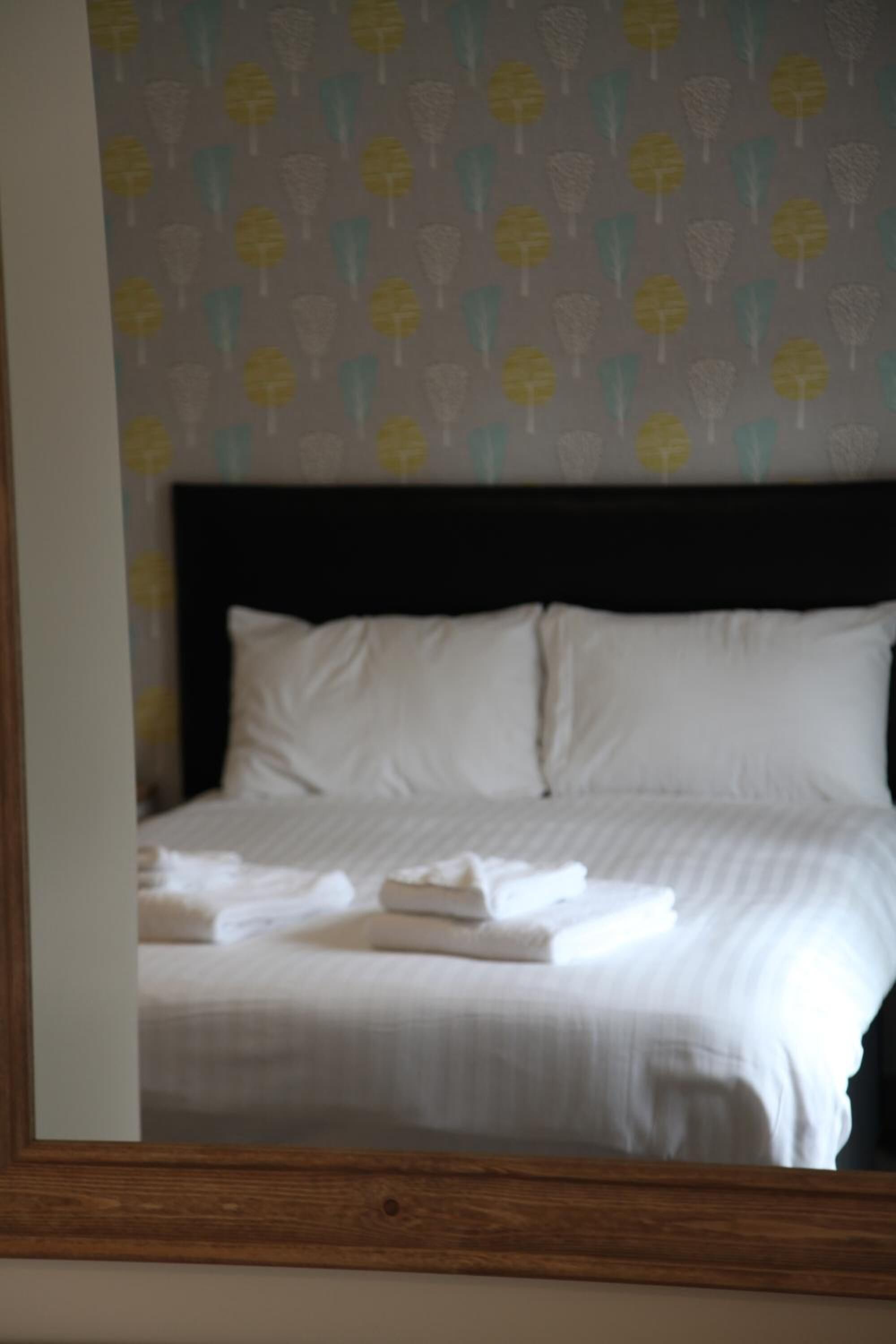 A neatly made bed with white linens and pillows, a dark headboard, and a patterned wallpaper with yellow and blue shapes.