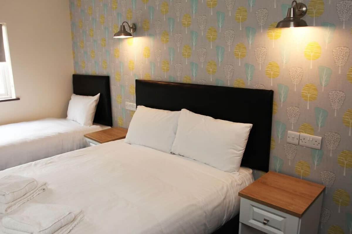 A hotel room with two single beds, a large bed, and a nightstand with a lamp.