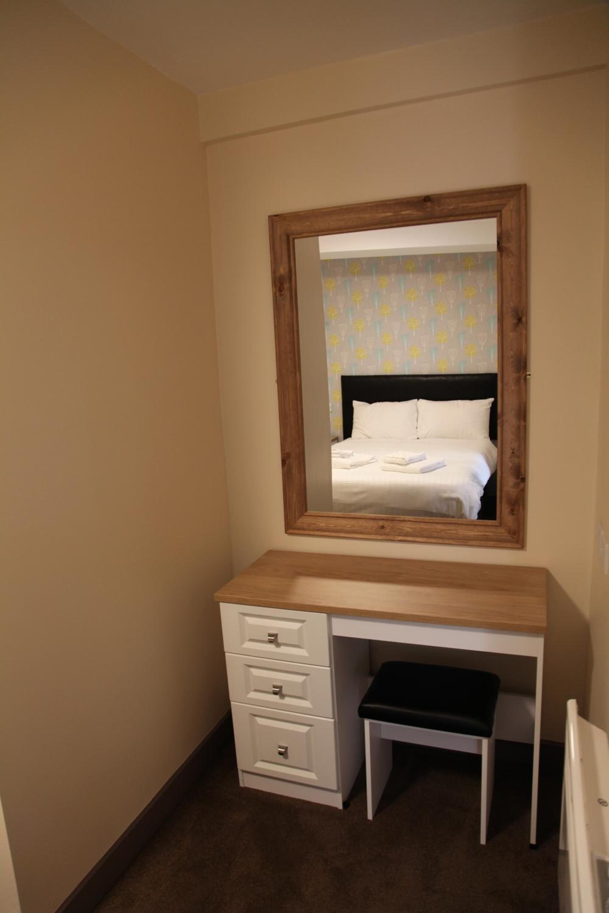 A bedroom with a wooden desk, a mirror, and a bed with white linens.