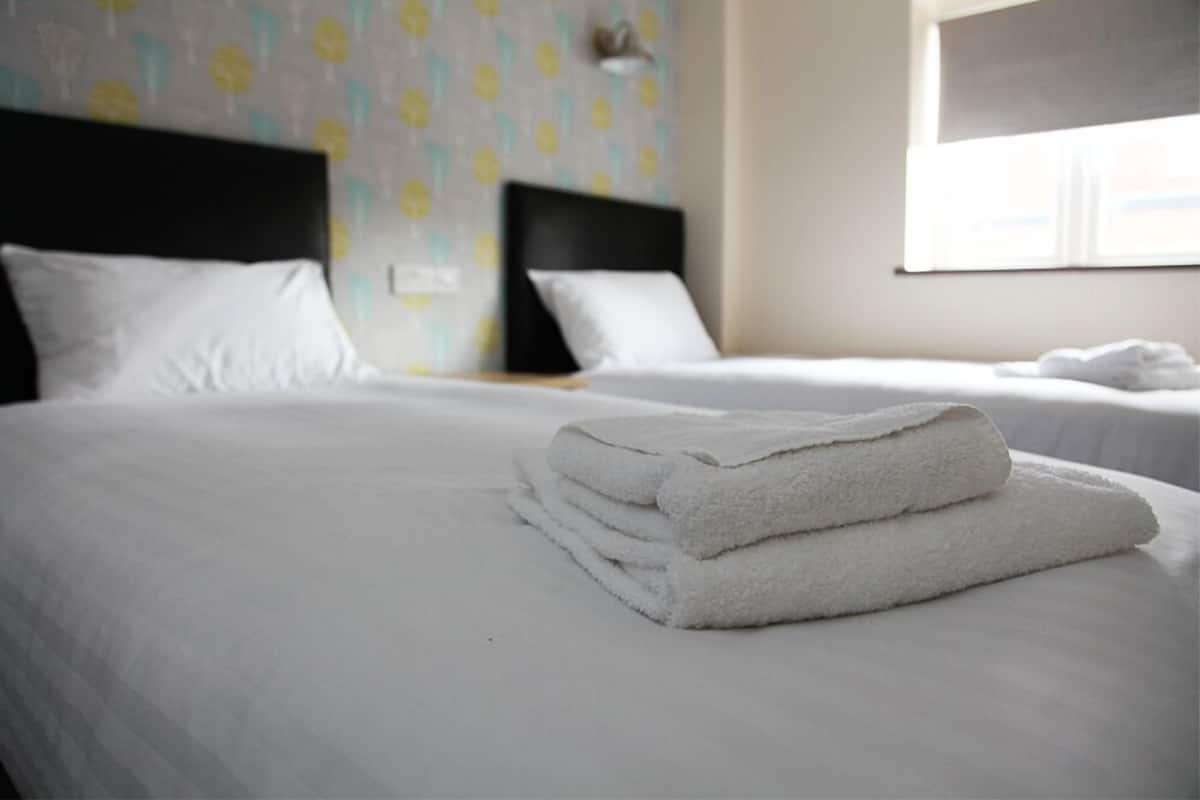 A hotel room with two beds, white linens, and a patterned wallpaper.