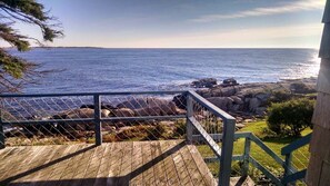 A wooden deck with a metal railing overlooking a rocky coastline and the ocean.