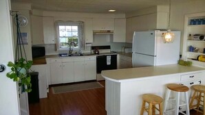A compact kitchen with white cabinets, a refrigerator, a sink, and a small window. - Quintessential Maine waterfront! (Biddeford)