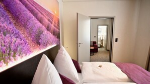 A hotel room with a large bed, a headboard with a floral mural, and a view into the hallway. - Bahnhof ERZINGEN hotel coffee  & more (Klettgau)