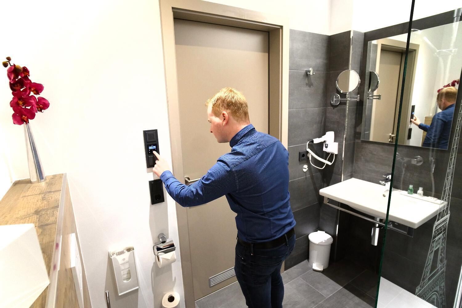 A man using a digital lock on a door in a modern bathroom with a sink and a mirror.