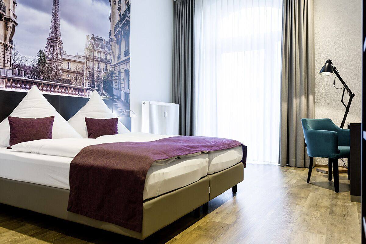 A hotel room with a bed, a chair, a lamp, and a view of the Eiffel Tower.