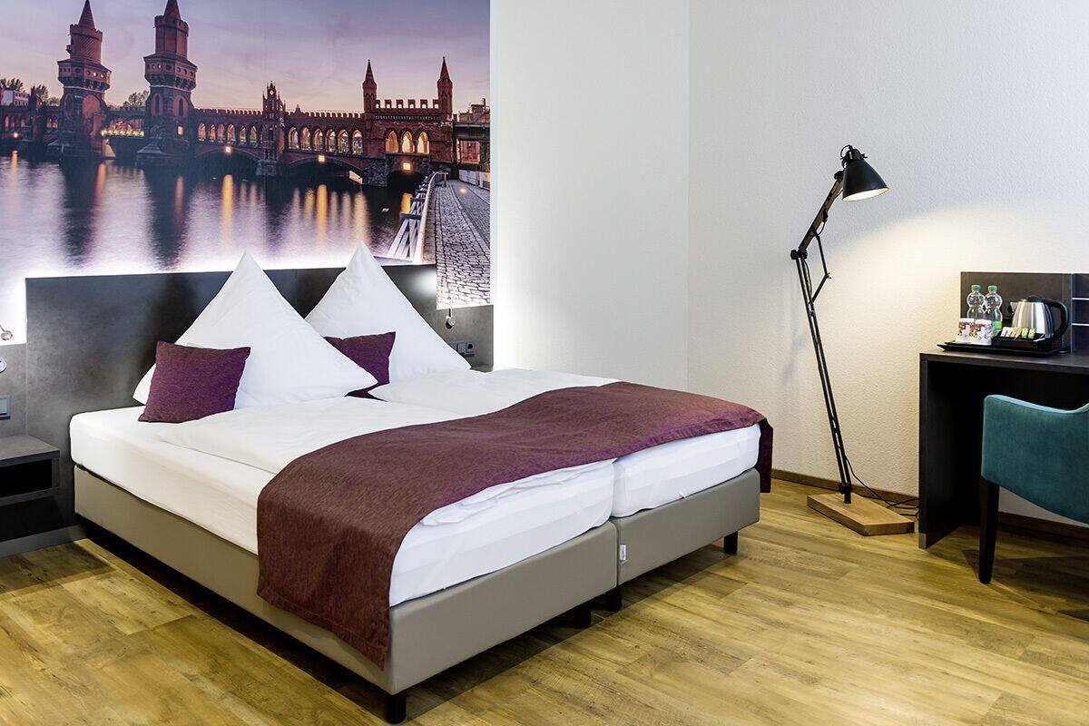 A modern hotel room with a large bed, a desk, a chair, and a nightstand.