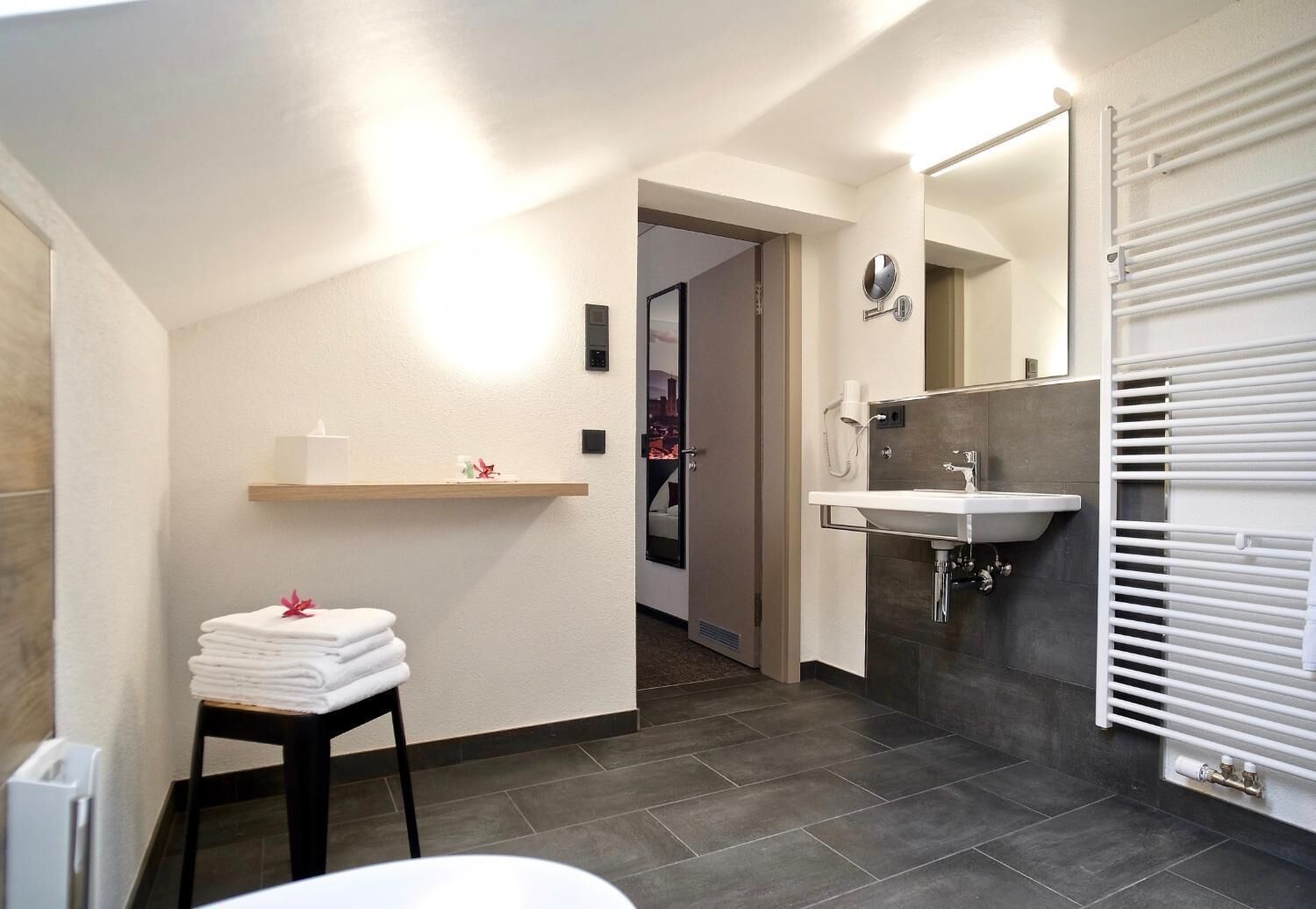 Un baño moderno con lavamanos, espejo y una pila de toallas.