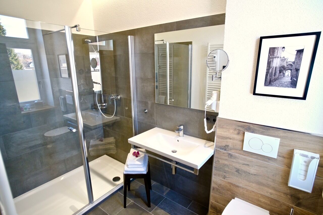 Un bany modern amb dutxa tancada amb vidre, un lavabo blanc i un moble de tocador de fusta.