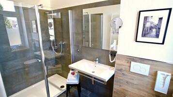 Un bany modern amb dutxa tancada amb vidre, un lavabo blanc i un moble de tocador de fusta.