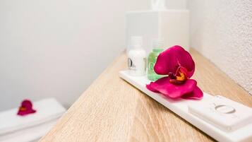 Ein Badezimmer mit einem Holzwaschtisch, einem weißen Seifenspender, einer grünen Flasche und einer pinkfarbenen Orchidee.