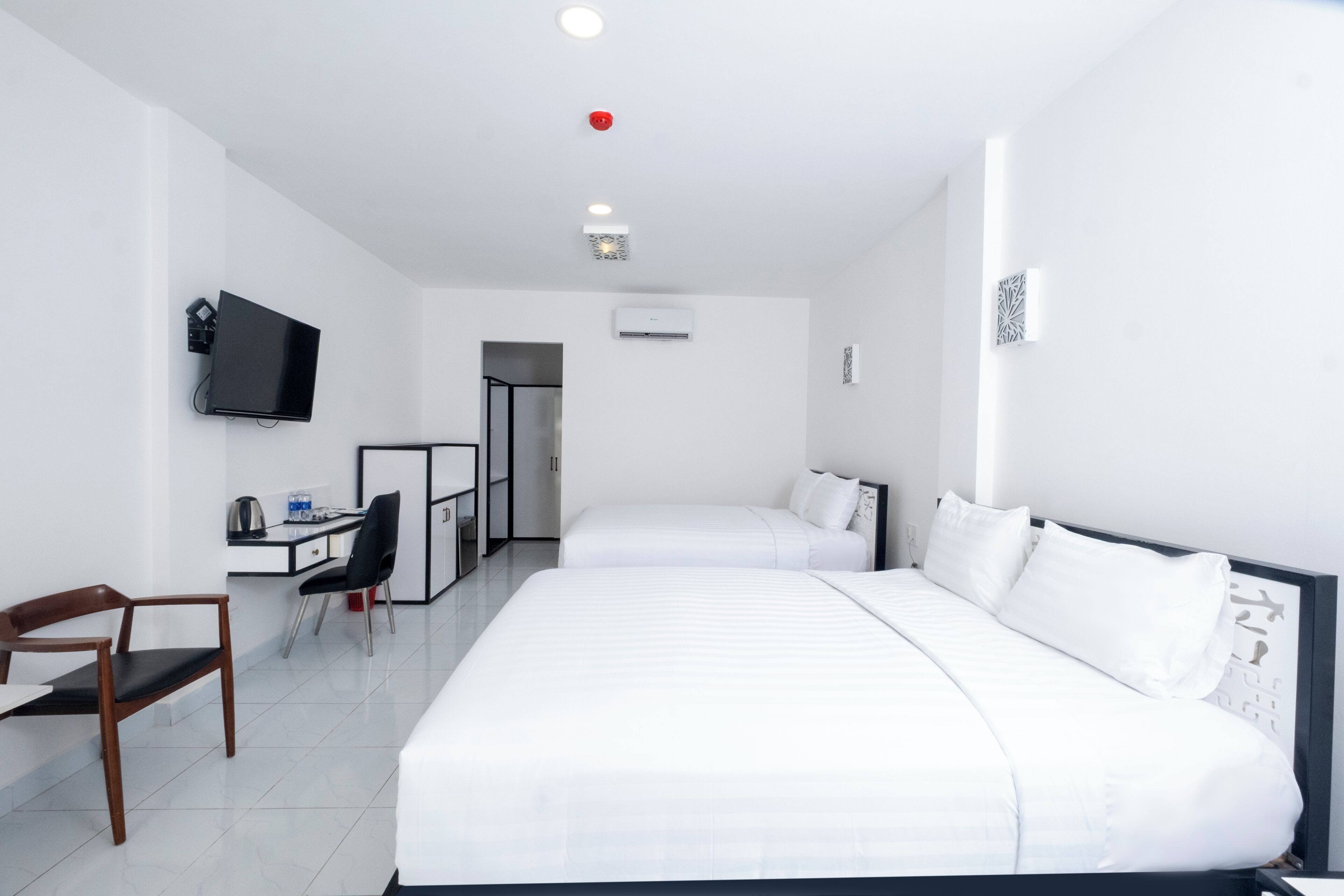 A hotel room with two beds, a desk with a chair, a television, and an air conditioning unit.