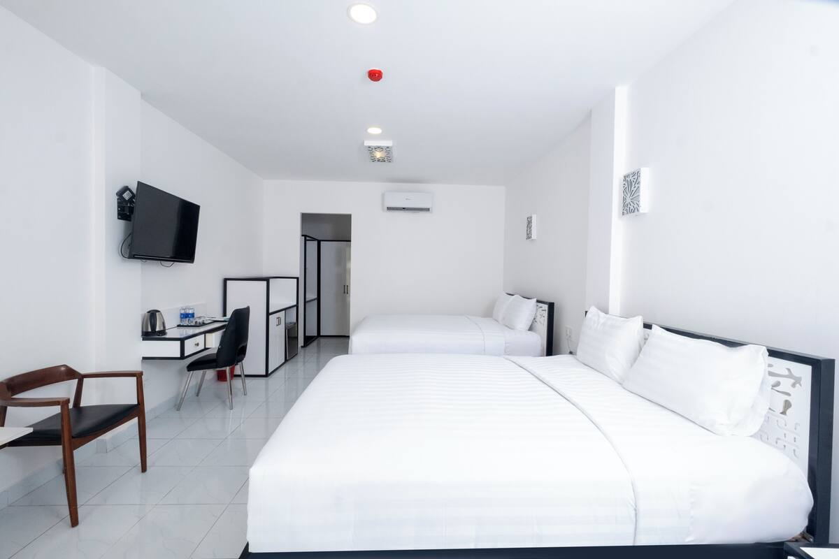 Een hotelkamer met twee bedden, een bureau met stoel, een televisie en een airconditioning.