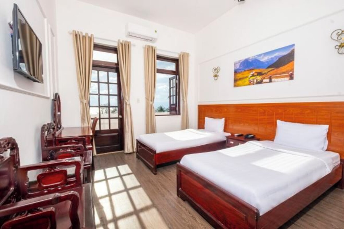 Une chambre d’hôtel avec deux lits, une tête de lit en bois, un bureau avec une chaise et un tableau au mur.