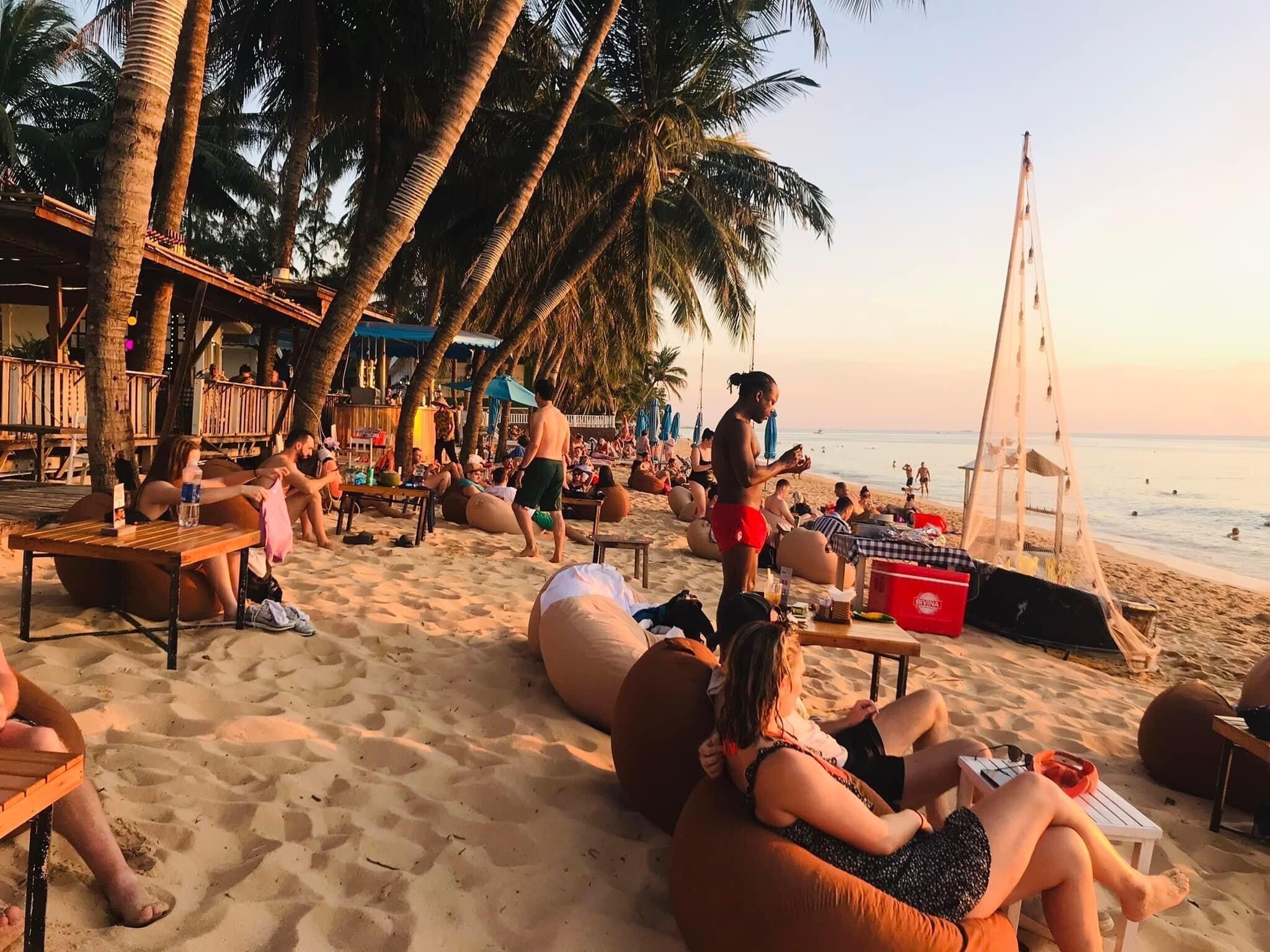 Ein Strand mit Palmen, Menschen, die auf Sitzsäcken entspannen, und einer Holzkonstruktion.