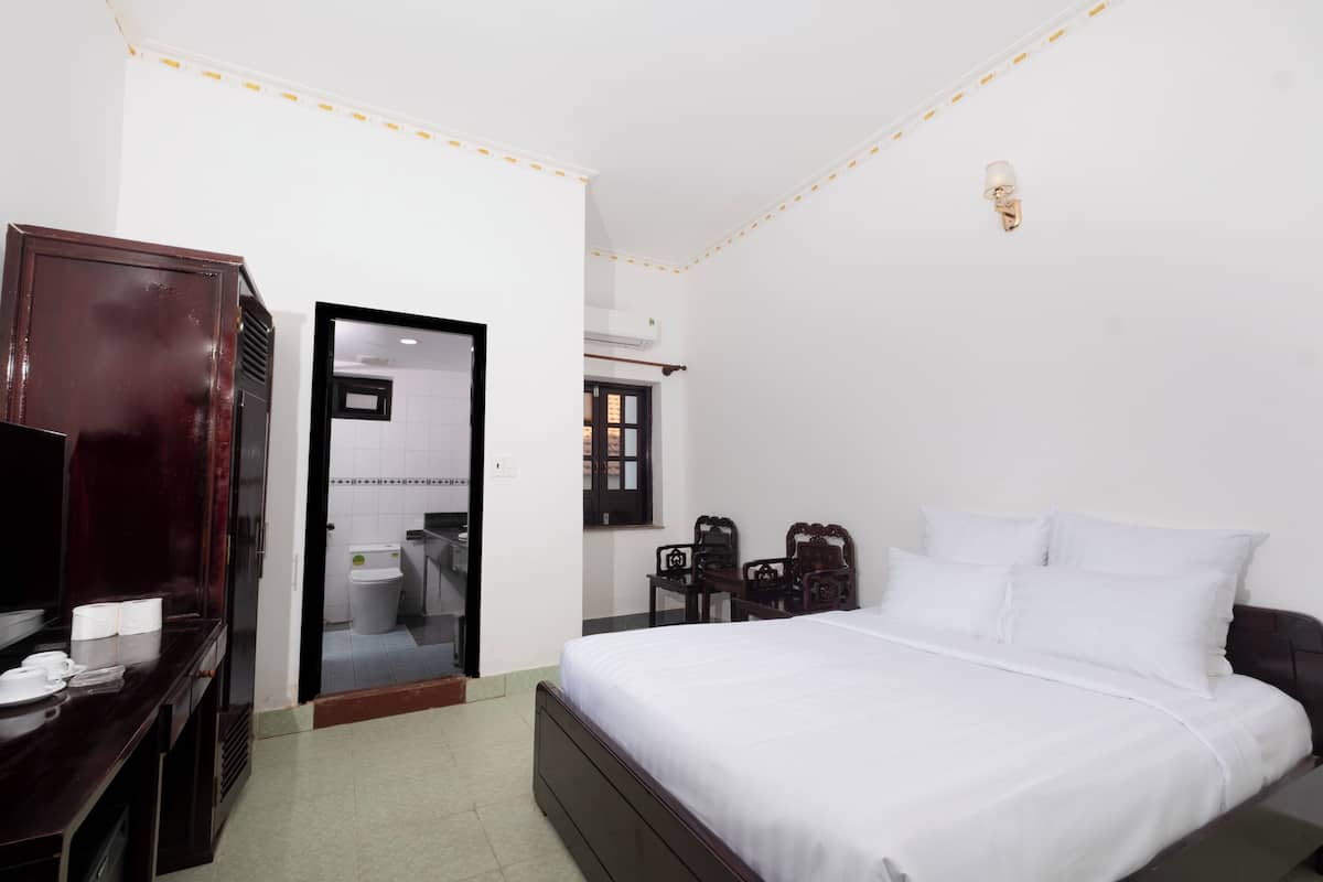 Een hotelkamer met een bed, een bureau met stoel, een garderobe en een zichtbare badkamer door een geopende deur.