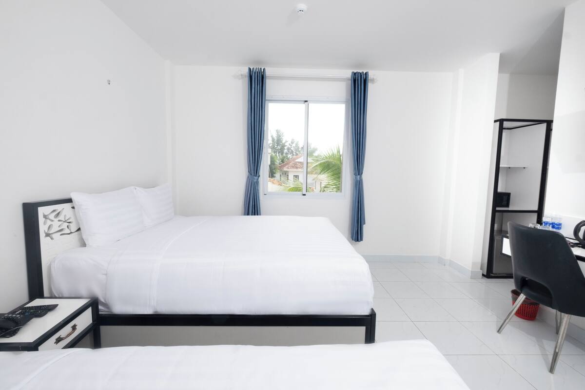 Een hotelkamer met een bed, bureau, stoel en raam met gordijnen.