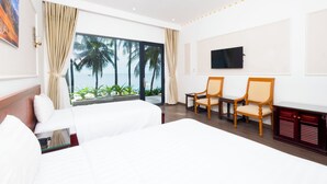 Ein Hotelzimmer mit zwei Betten, einem Fernseher und Blick auf Palmen und das Meer.