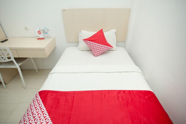 A bed with a red and white patterned pillow, a white desk with a remote control, and a chair. - Hotel O Lapan Lapan (Banjarmasin)