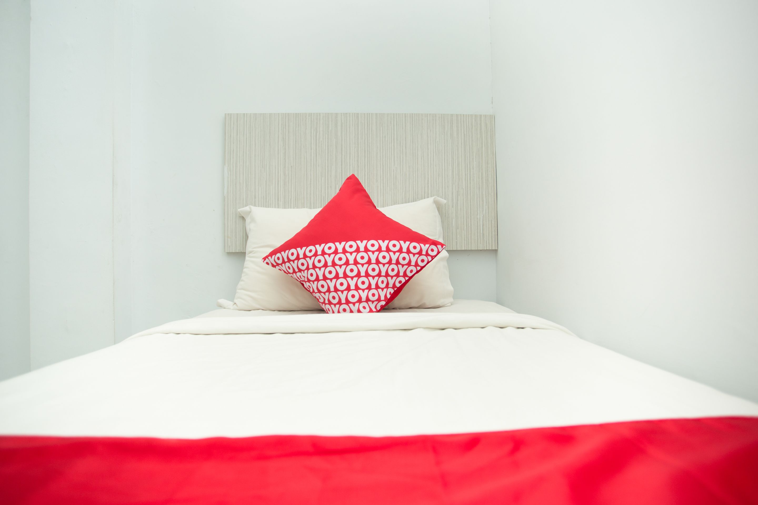 A bed with a white headboard and a red and white pillow.