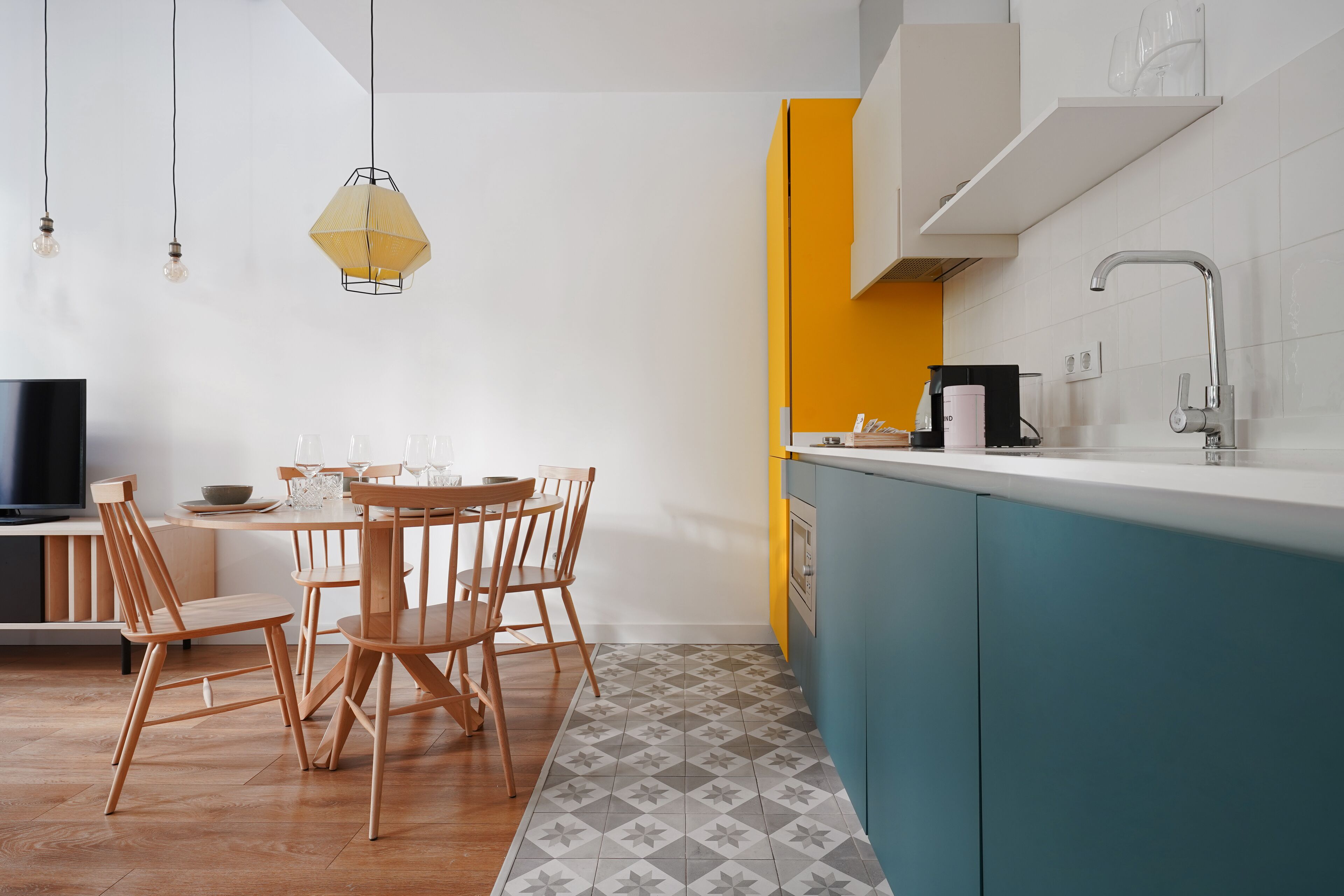 A modern kitchen with a dining area, featuring a wooden table and chairs, a built-in stove, and a yellow accent wall.