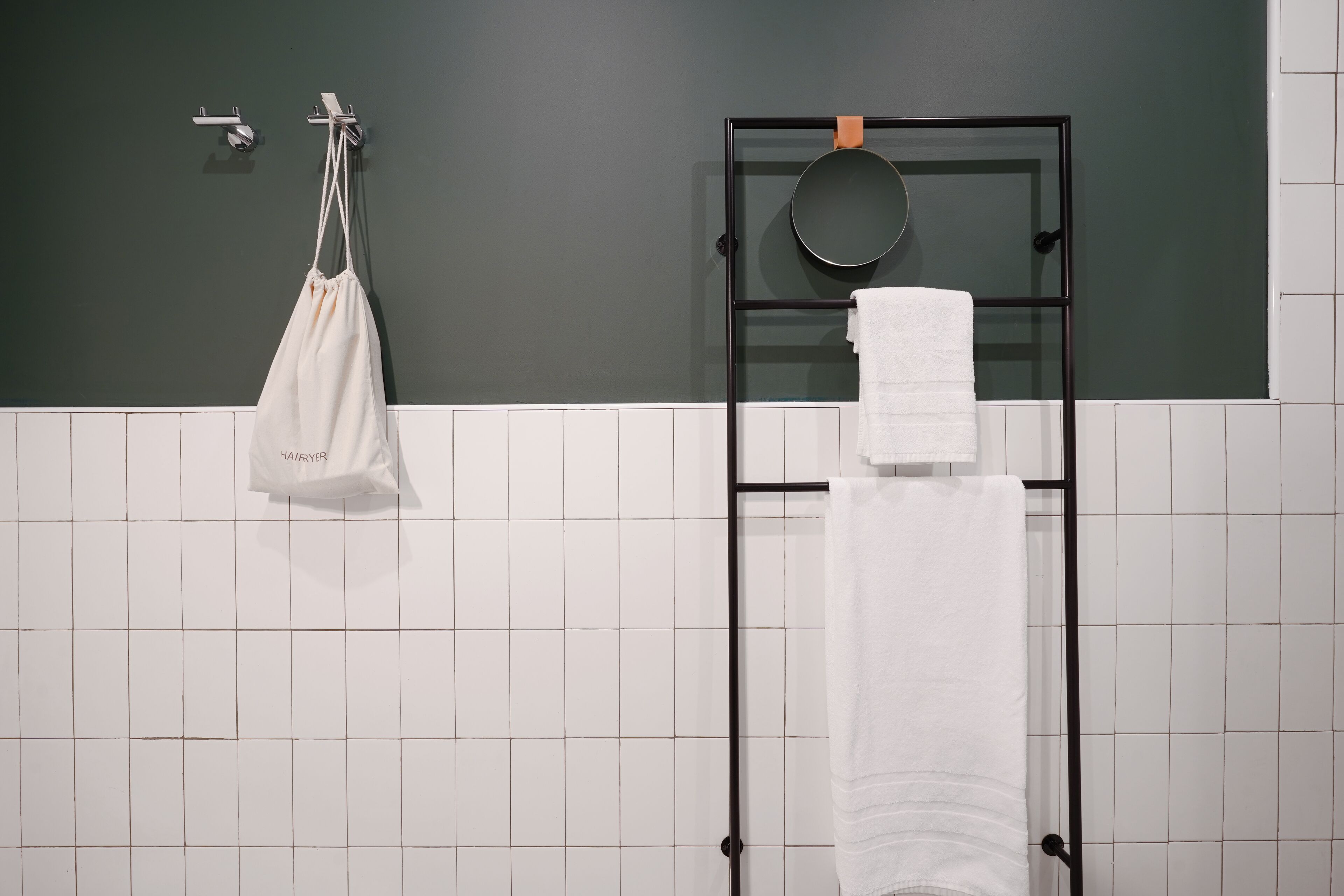 Un baño con un toallero negro, una bolsa colgada y una toalla blanca.