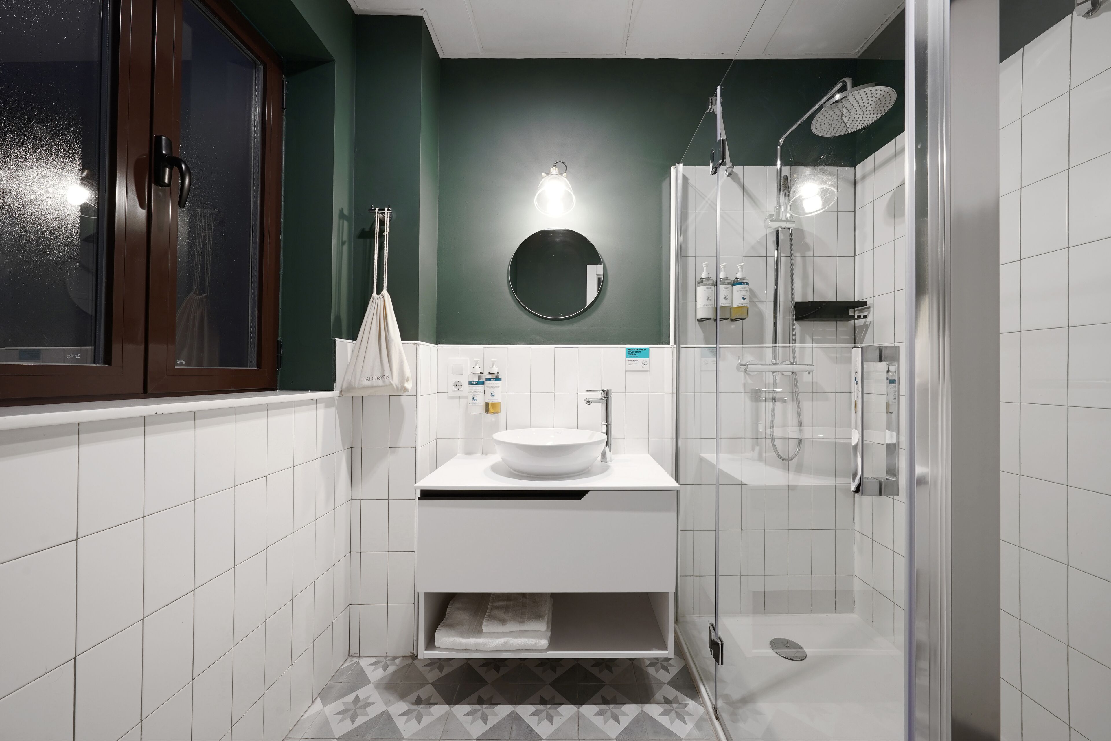 A modern bathroom with a white sink, a round mirror, and a glass-enclosed shower.