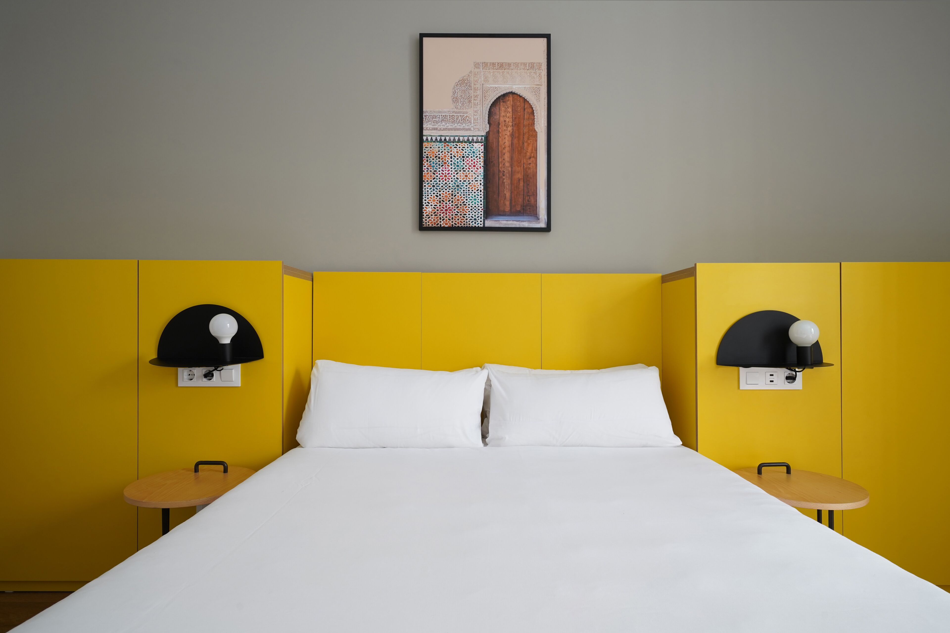 Habitació d'hotel amb un llit, dues taules de nit i una làmpada penjada a la paret.