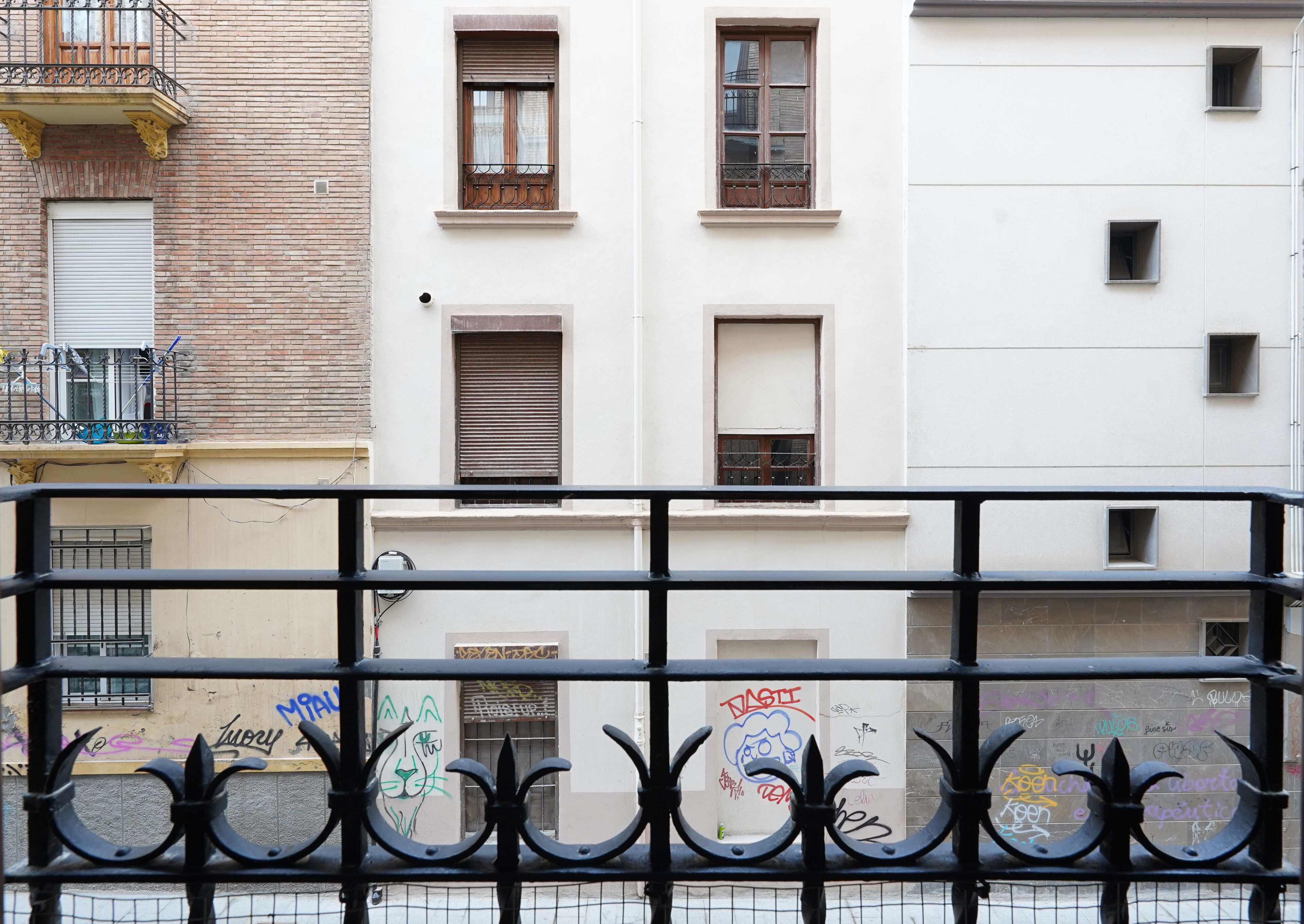 Ein Gebäude mit mehreren Fenstern, von denen einige mit Rollläden versehen sind, und einem Balkon mit Metallgeländer.